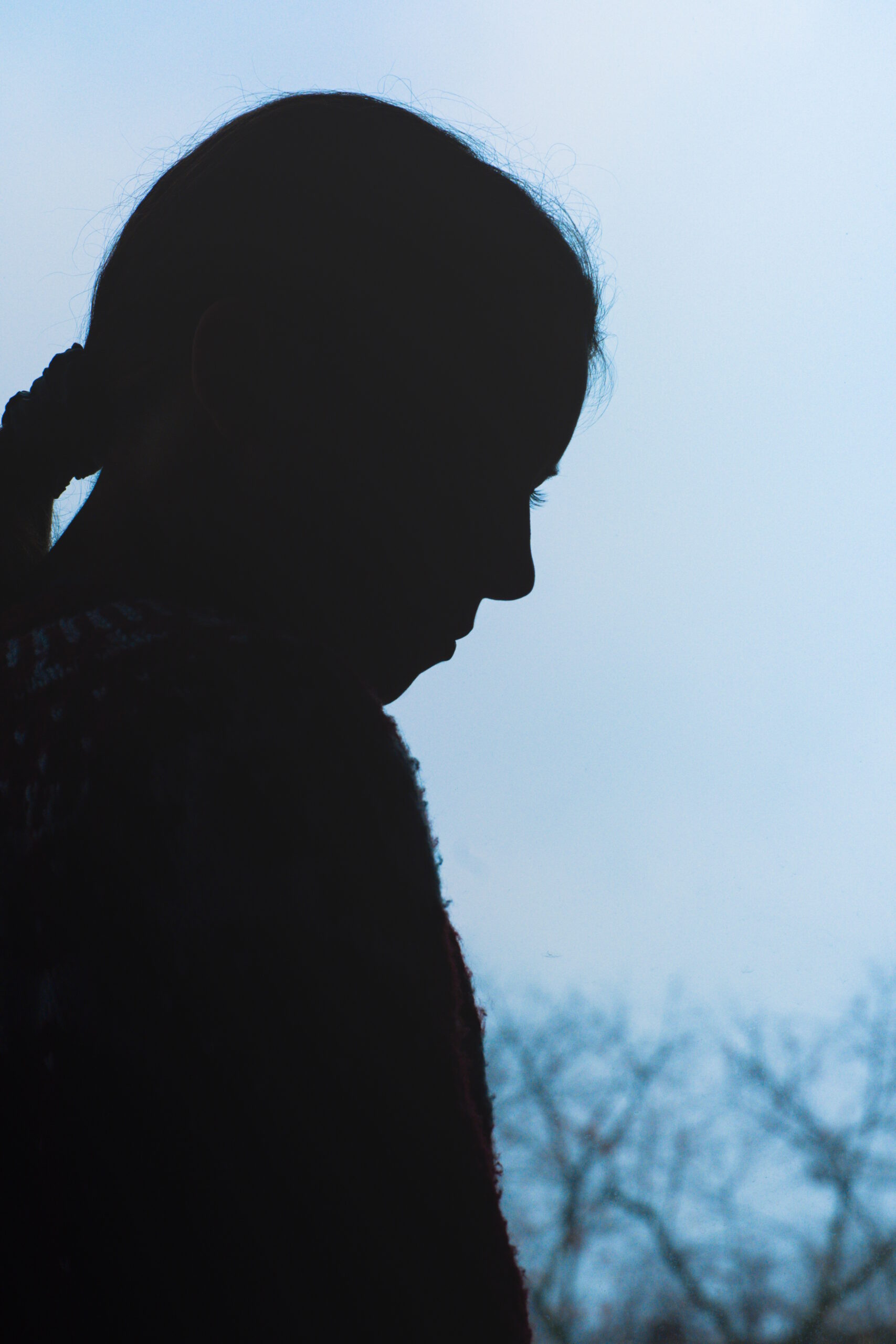 Silhouette of a woman from the side. Some branches in the lower right corner.