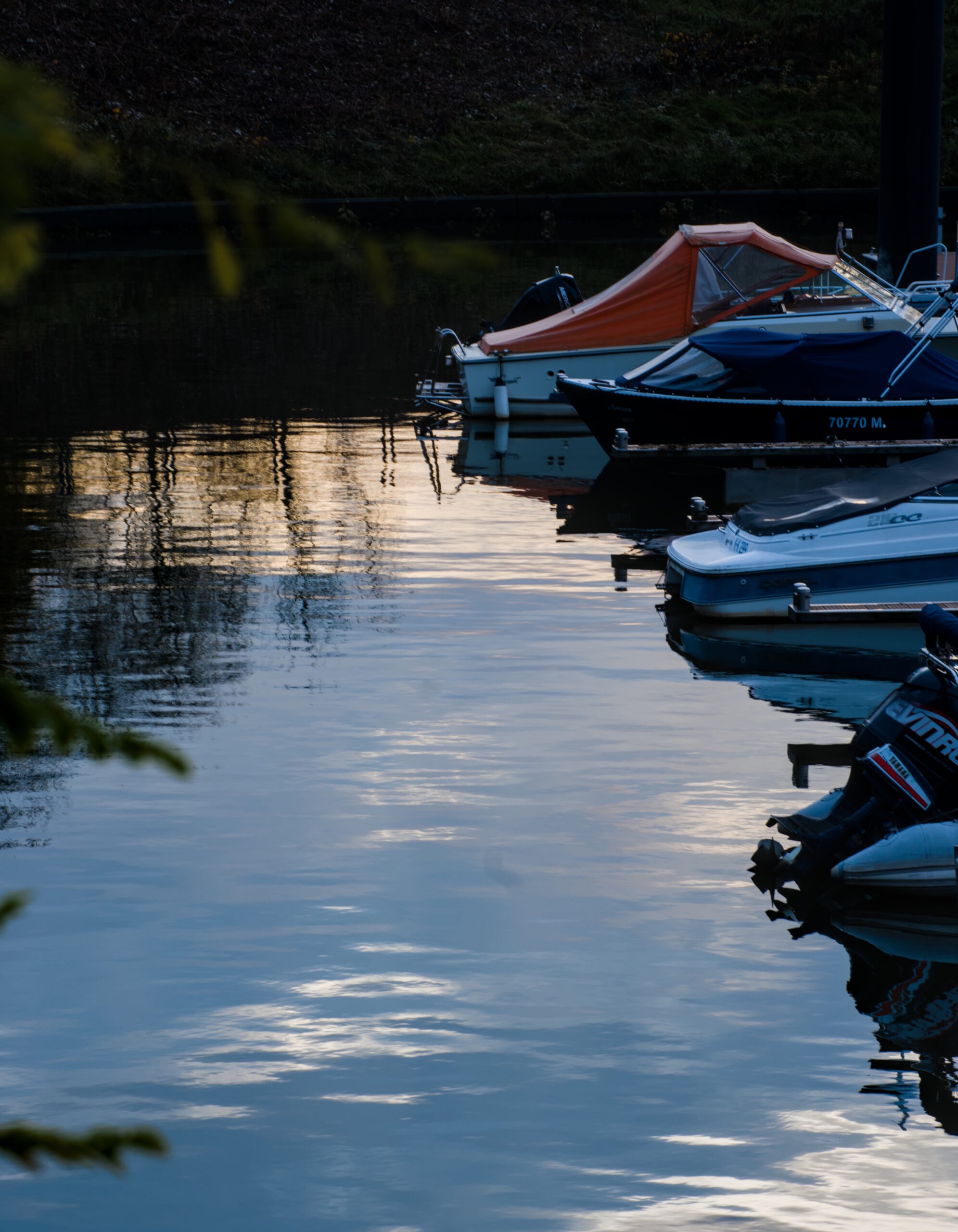 Boats parked in calm water. Evening golden and cloudy sky is reflected in the water.