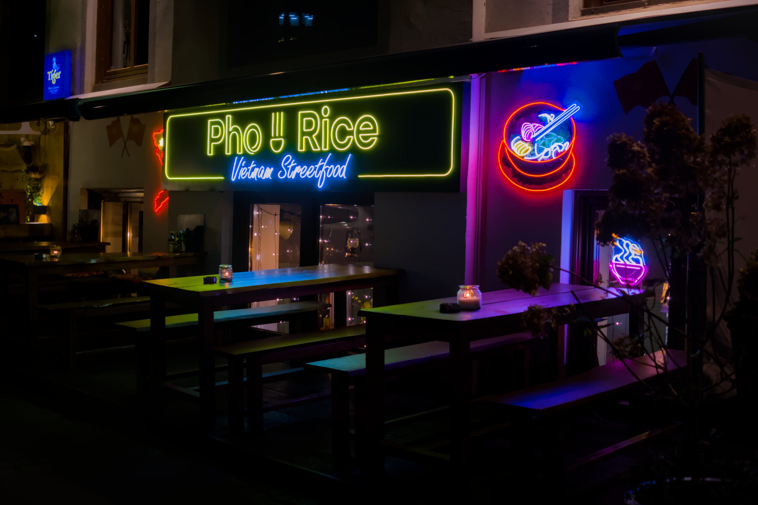 Outside view of a vietnamese restaurant in the dark. Big neon sign with the text "Pho Rice Vietnam Streetfood".