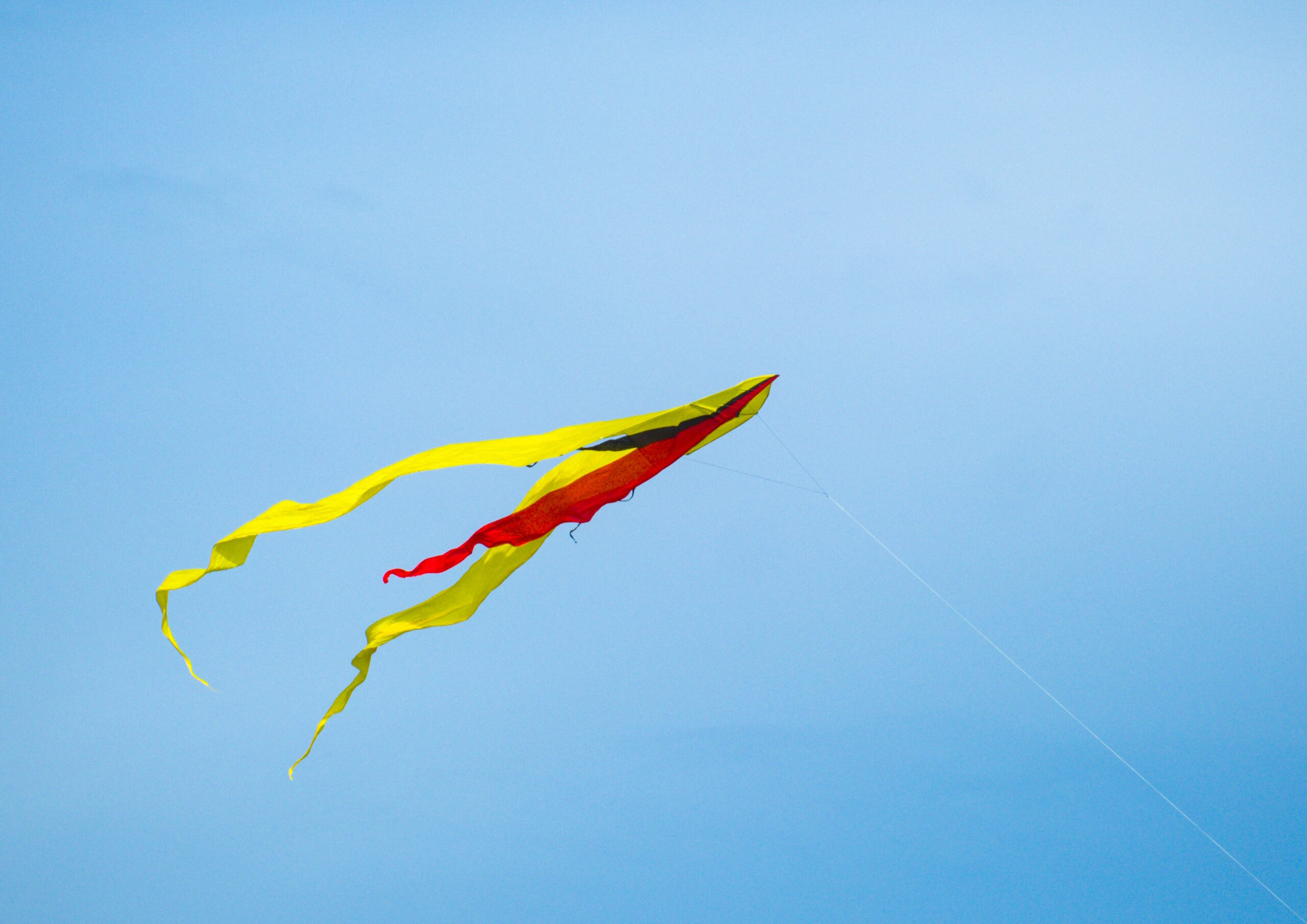 A red and yellow kite flying, against a blue sky
