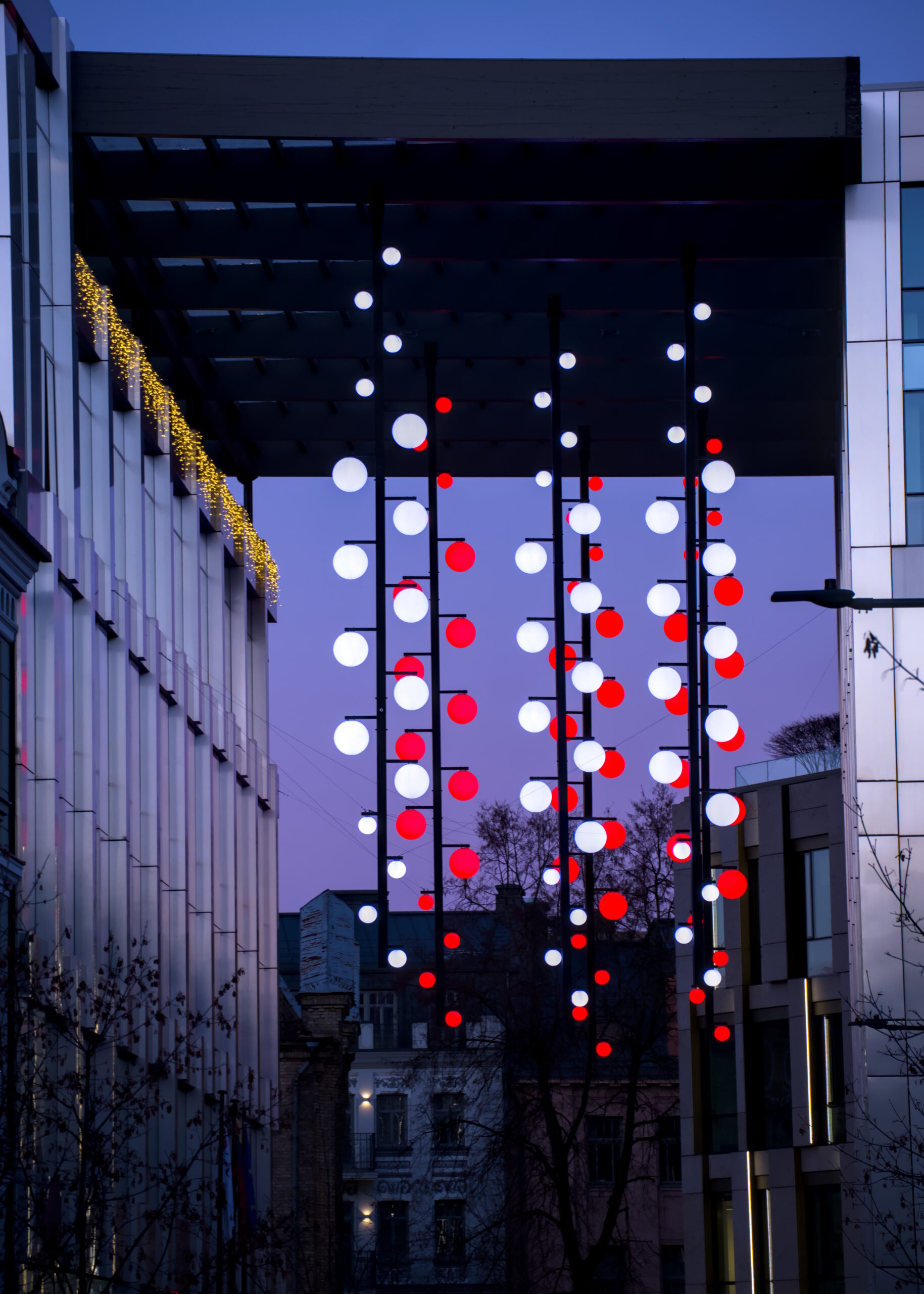 Hanging round white and red bulbs from a roof canopy between two 5 story buildings